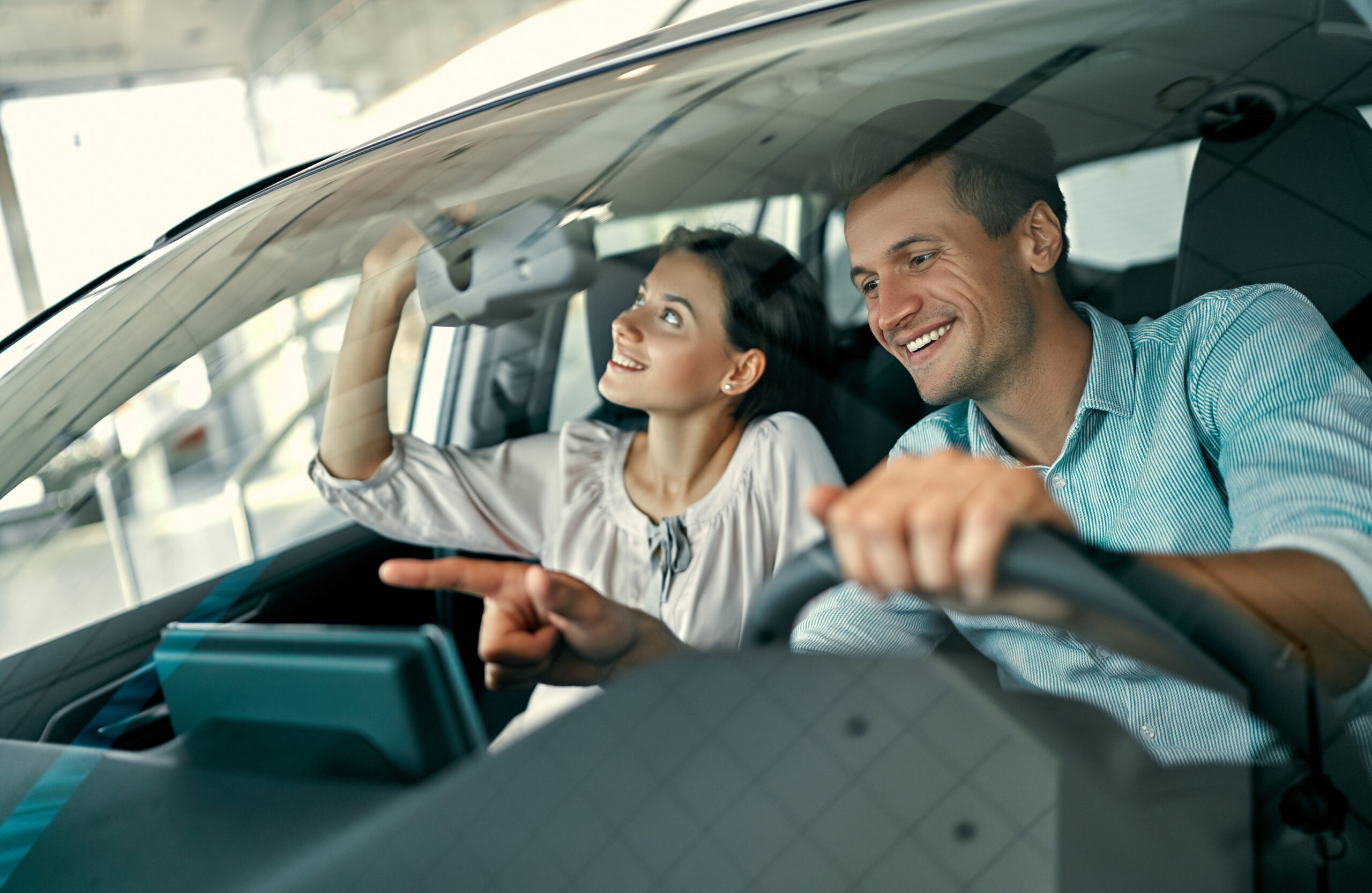 A young couple is sitting in a new car and inspecting it. Buying and renting cars at a car dealership.